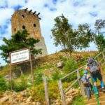 Turysta z dzieckiem wychodzący po schodach prowadzących do schroniska Wysoki Kamień, w tle kamienna wieża widokowa