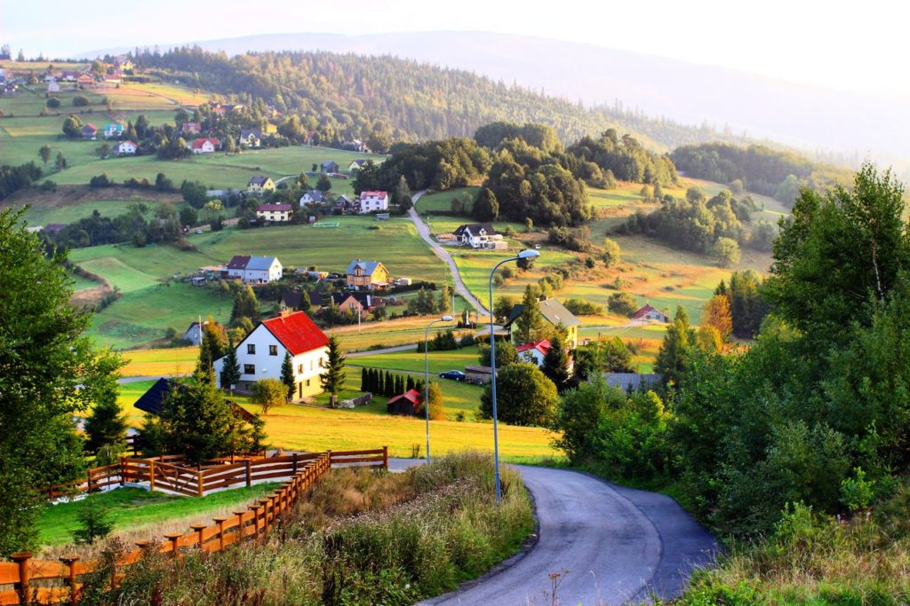 Widok na wieś Koniaków o poranku, w tle domy, góry, drzewa oraz droga asfaltowa