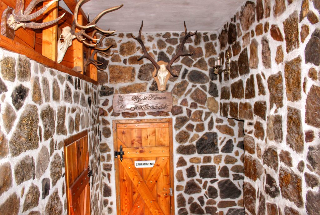 Wnętrze Schroniska Wysoki Kamień w Górach Izerskich, kamienne ściany, drewniane drzwi, na ścianie wiszące poroże
