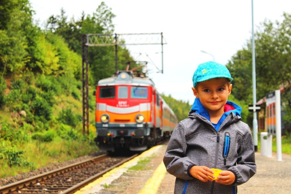 dziecko stojące na Dworcu w Szklarskiej Porębie Dolnej na tle zowego pociągu oraz torów kolejowych