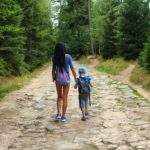 kobieta idąca z dzieckiem szeroką kamienistą drogą leśną