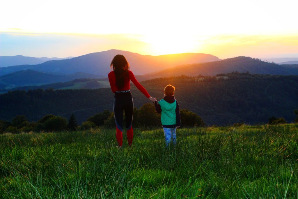 kobieta trzymająca za rękę dziecko, na Polanie Kotarskiej na tle zachodzącego słońca za górami