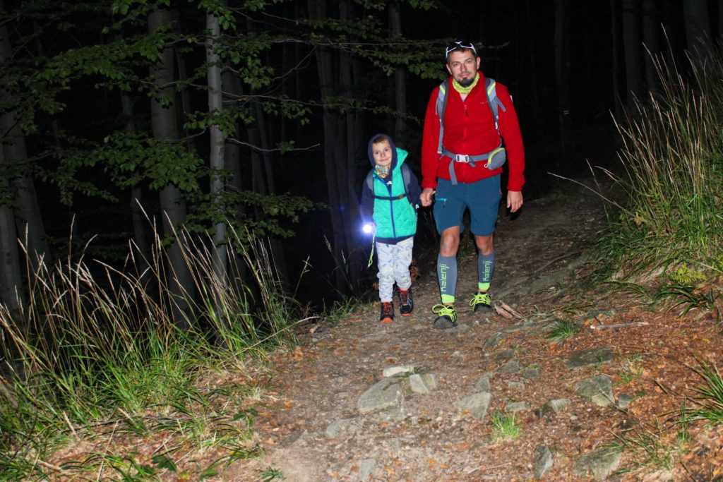 mężczyzna z dzieckiem idący przez ciemny las, chłopiec oświetla drogę latarką