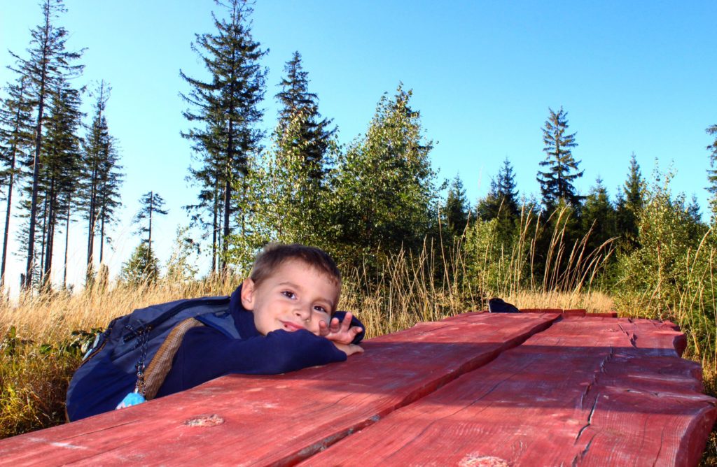 uśmiechnięte dziecko odpoczywające przy drewnianym stole w pobliżu Białego Krzyża, drzewa, niebieskie niebo