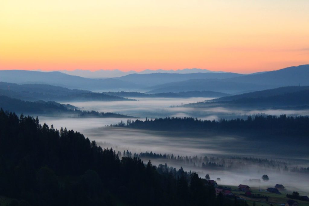 wschodzące słońce poniżej szczytu Ochodzita, morze mgieł zalewające domy, drzewa, w tle krajobraz górski, Tatry