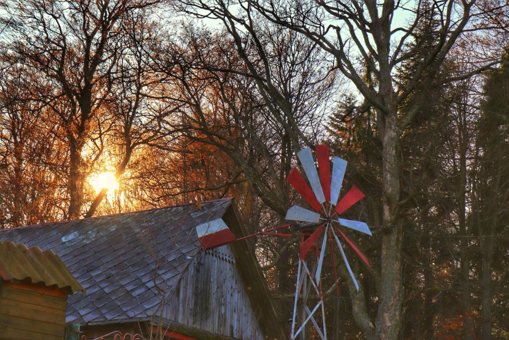 Dachy domków znajdujących się na Polanie Zabawa w Beskidzie Śląskim, czerwono - biały wiatrak, słońce przebijające się zza drzew