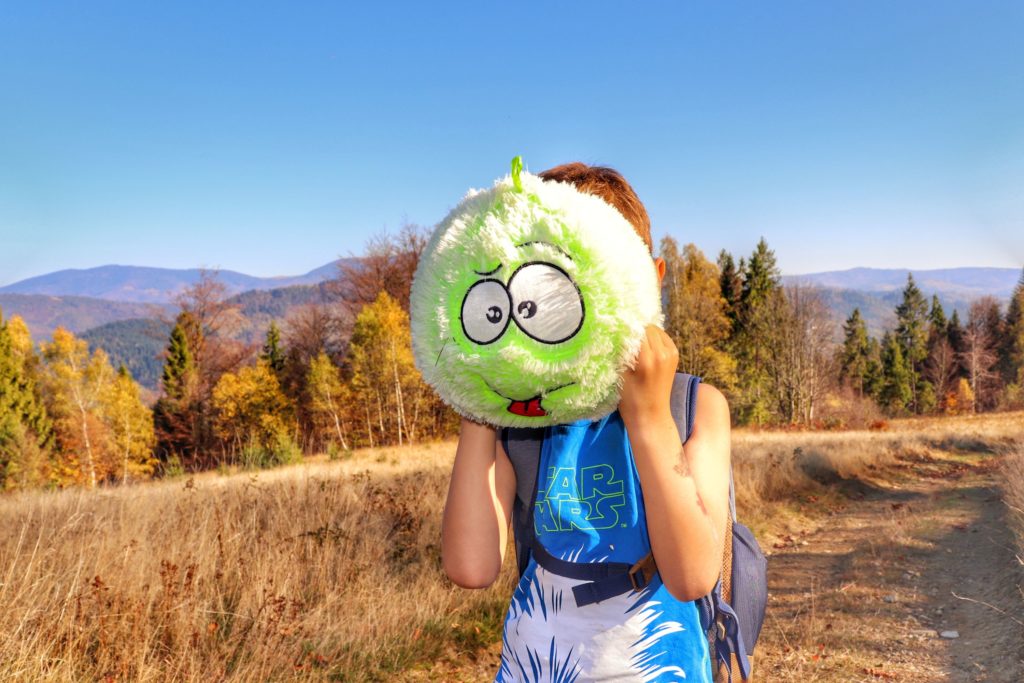 Dziecko zakrywające twarz włochatą piłką z oczami na Polanie Zabawa, w koło jesienna sceneria