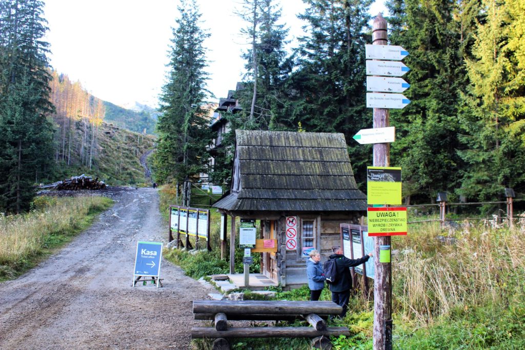 Kasa Tatrzańskiego Parku Narodowego na początku zielonego szlaku na Kasprowy Wierch, szeroka, utwardzona droga, turyści zerkający na mapę