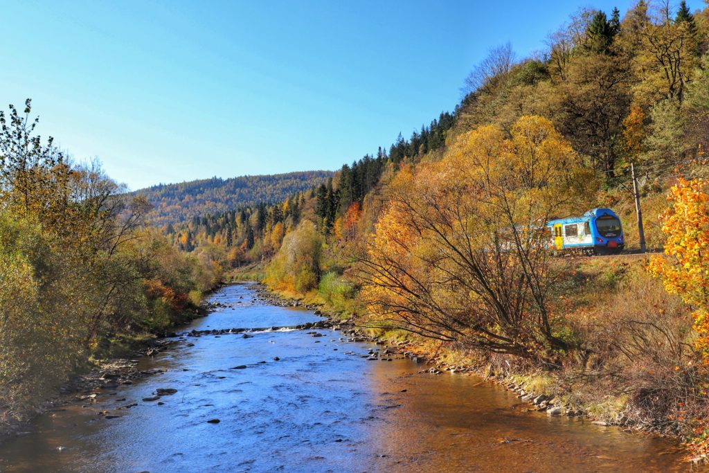 Rzeka Soła w Rajczy Dolnej, jesień, kolorowe liście na drzewach, pociąg, w tle krajobraz górski