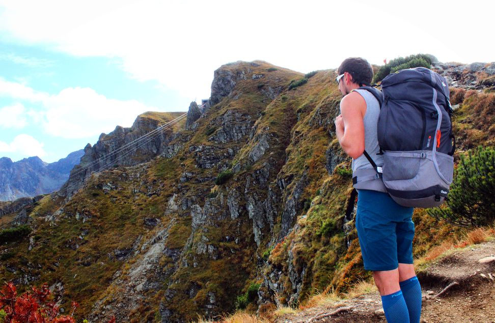 mężczyzna z plecakiem turystycznym stojący pod szczytem Kasprowy Wierch patrzący na góry
