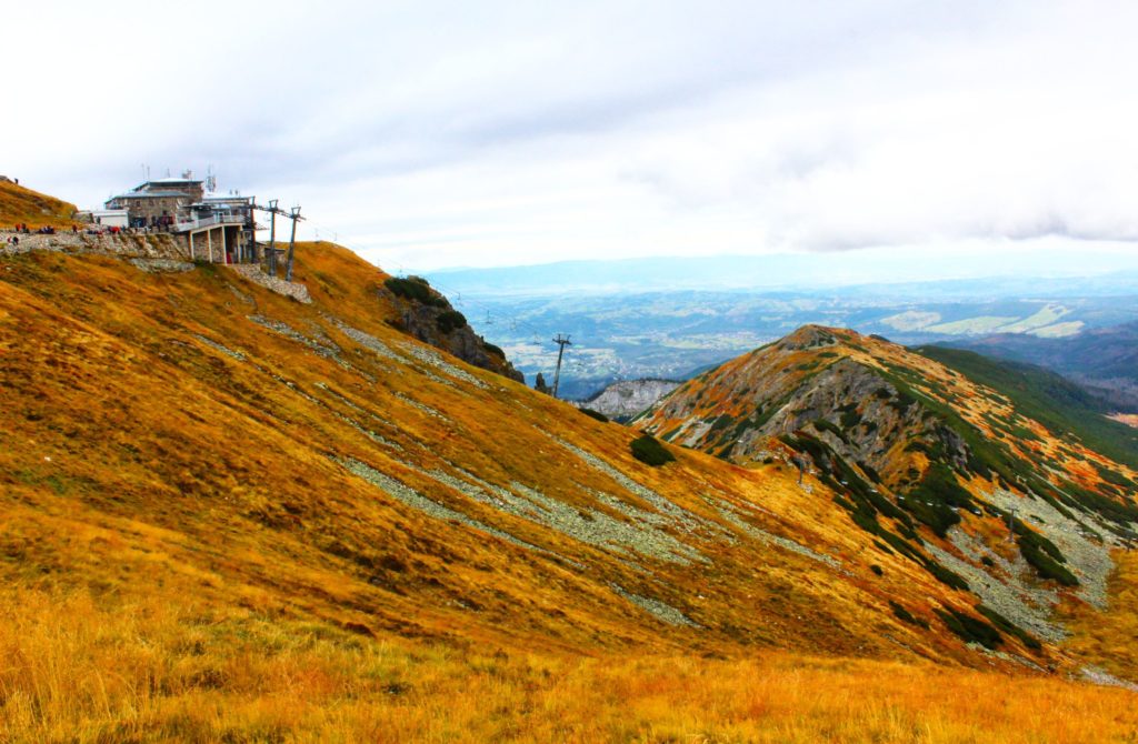 widok na górną stację kolejki na Kasprowy Wierch, żółta trawa, w tle tatrzańskie szczyty