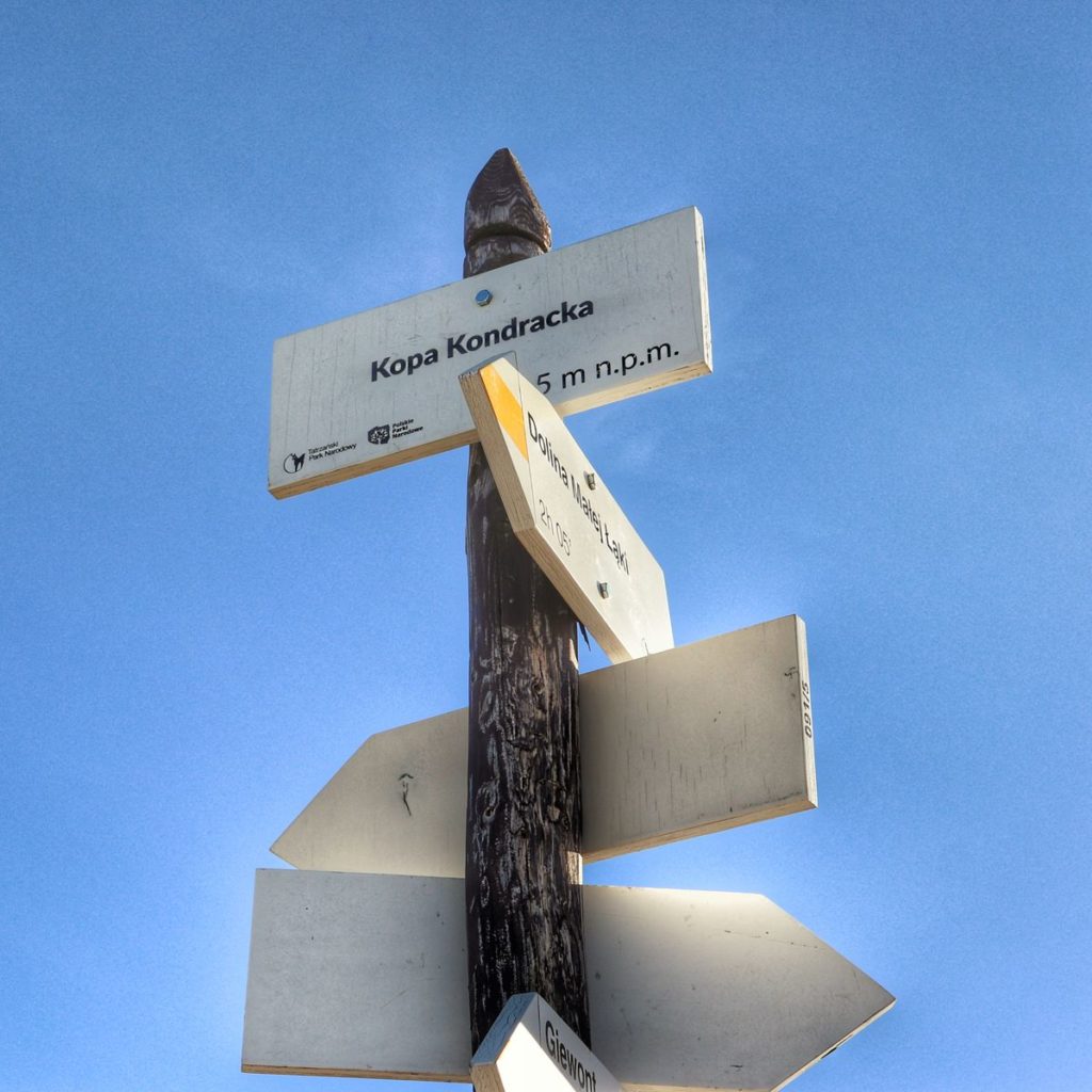 Biała tabliczka na tle niebieskiego nieba oznaczająca szczyt Kopa Kondracka 2005 metrów