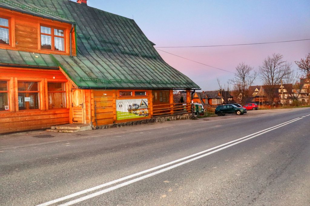 Droga w mieście Zakopane, ulica Cyrhla, po prawej stronie drewniany budynek restauracji noszącej nazwę Siedem Kotów