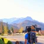 Dziecko idące za rękę z tatą lewą stroną ulicy - poboczem, w tle tatrzańskie szczyty