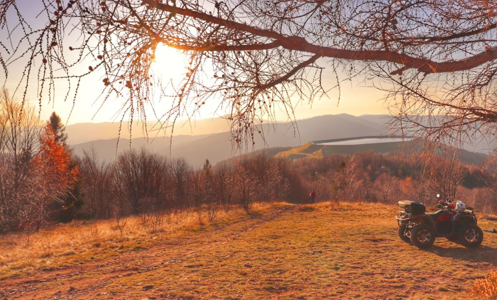Szczyt Kiczera w jesiennych barwach, zachodzące słońce, drzewa, widoczny w oddali zbiornik retencyjny na Górze Żar, po prawej stronie zaparkowany quad