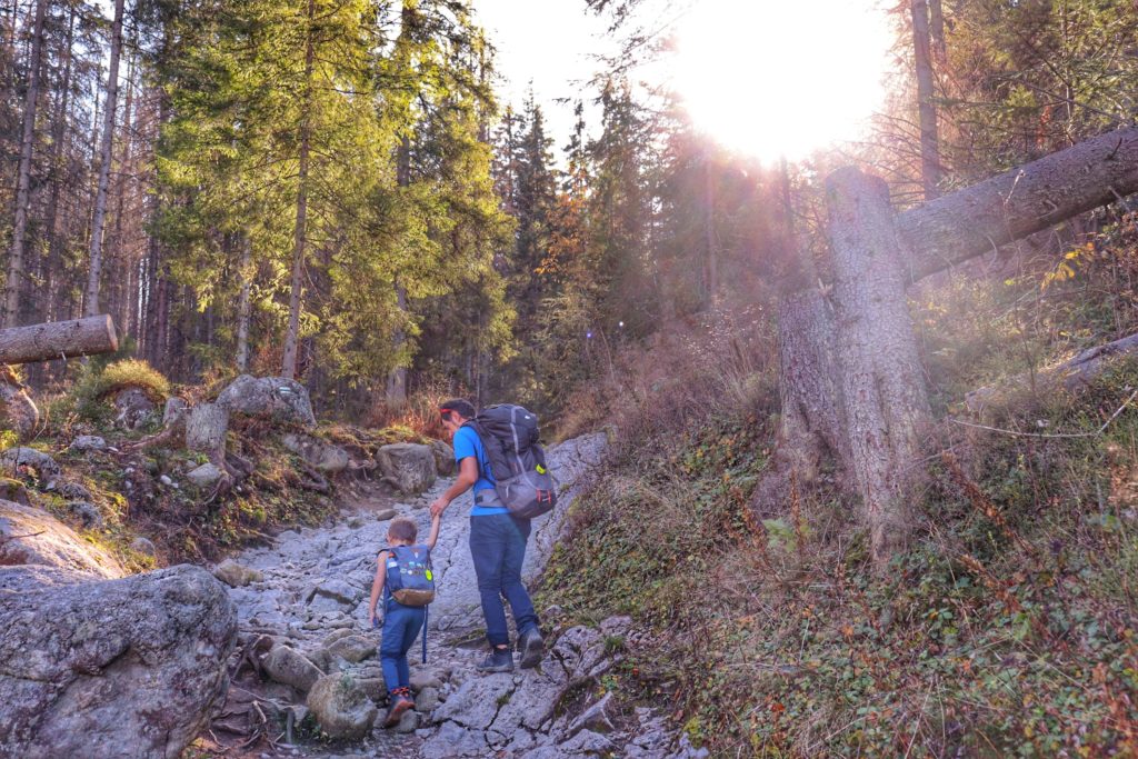 dziecko z tatą pokonujące strome, skalne podejście na tatrzańskim szlaku, na niebie pełne słońce