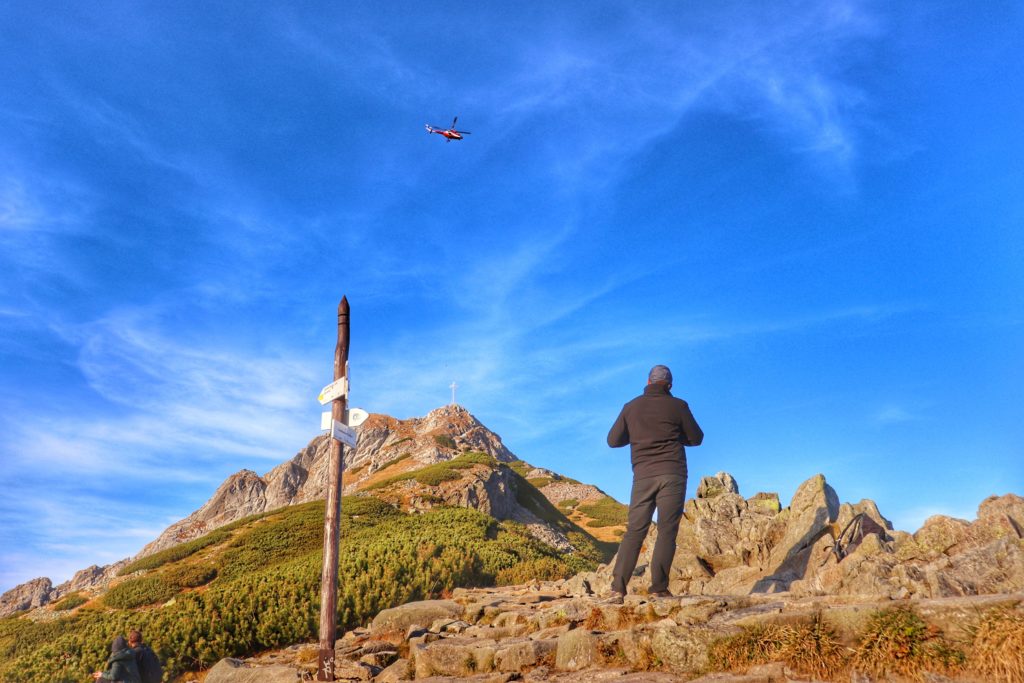 mężczyzna patrzący na helikopter Tatrzańskiego Parku Narodowego latającego nad Giewontem, niebieskie niebo