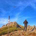 mężczyzna patrzący na helikopter Tatrzańskiego Parku Narodowego latającego nad Giewontem, niebieskie niebo