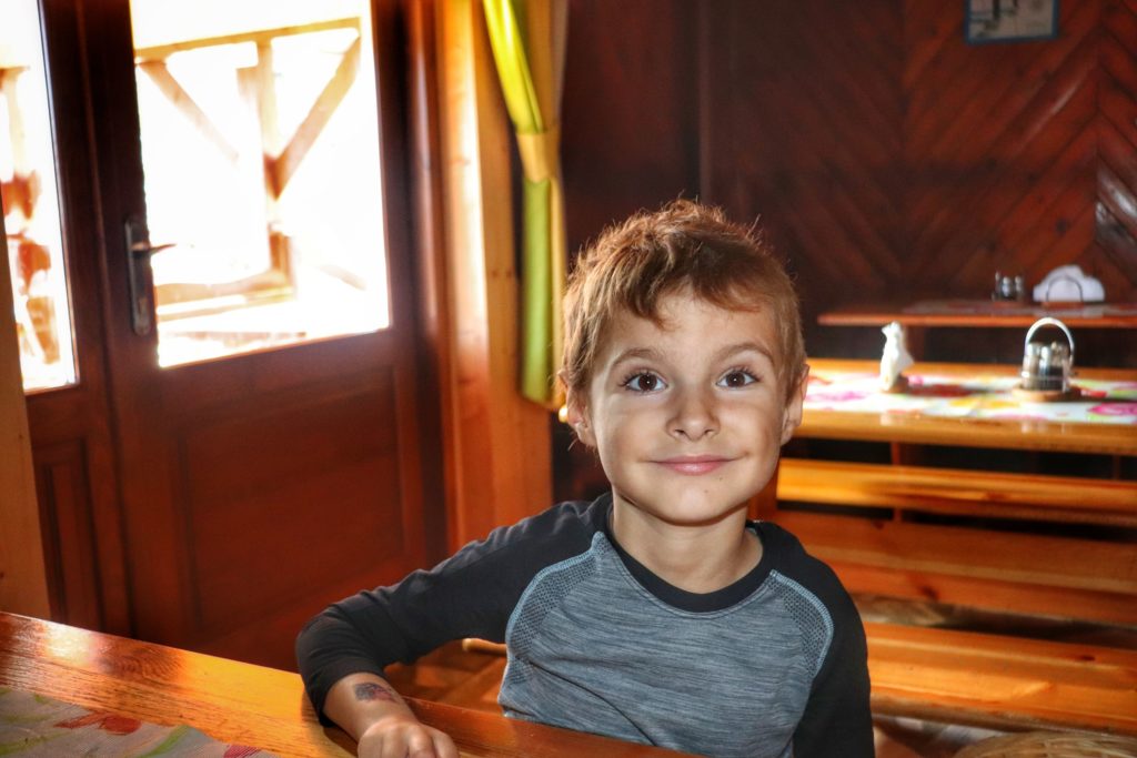 uśmiechnięte dziecko siedzące przy drewnianym stole w Schronisku na Hali Krupowej