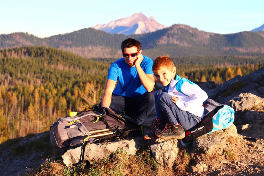 uśmiechnięty chłopiec siedzący z tatą na skałach, z tyłu widoczne tatrzańskie szczyty