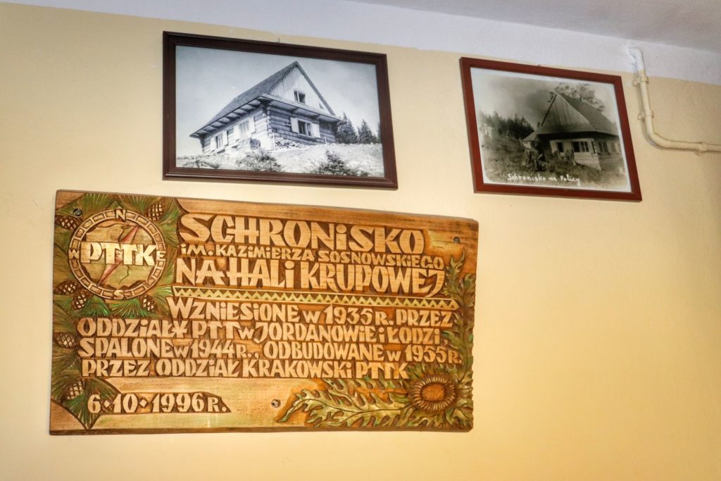 Drewniana tablica wisząca w schronisku na Hali Krupowej, opisany rok zalożenia 1935 rok, obrazy przedstawiające schronisko z przed lat