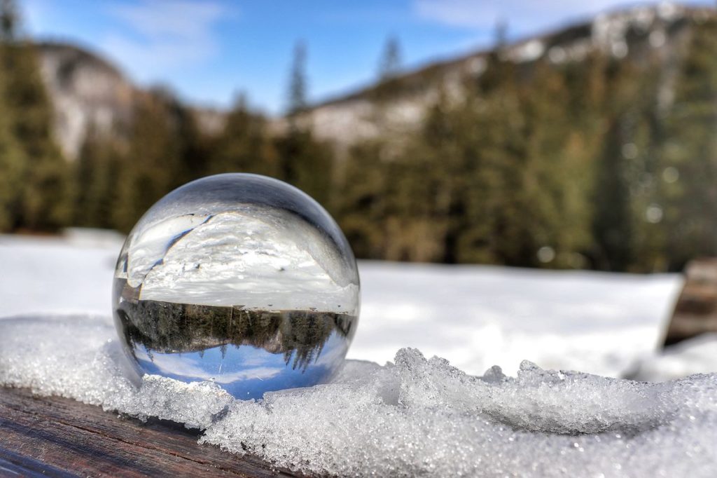 Szklana kula leżąca na drewnianym, zaśnieżonym stole, w której odbija się Polana Olczyska zimą