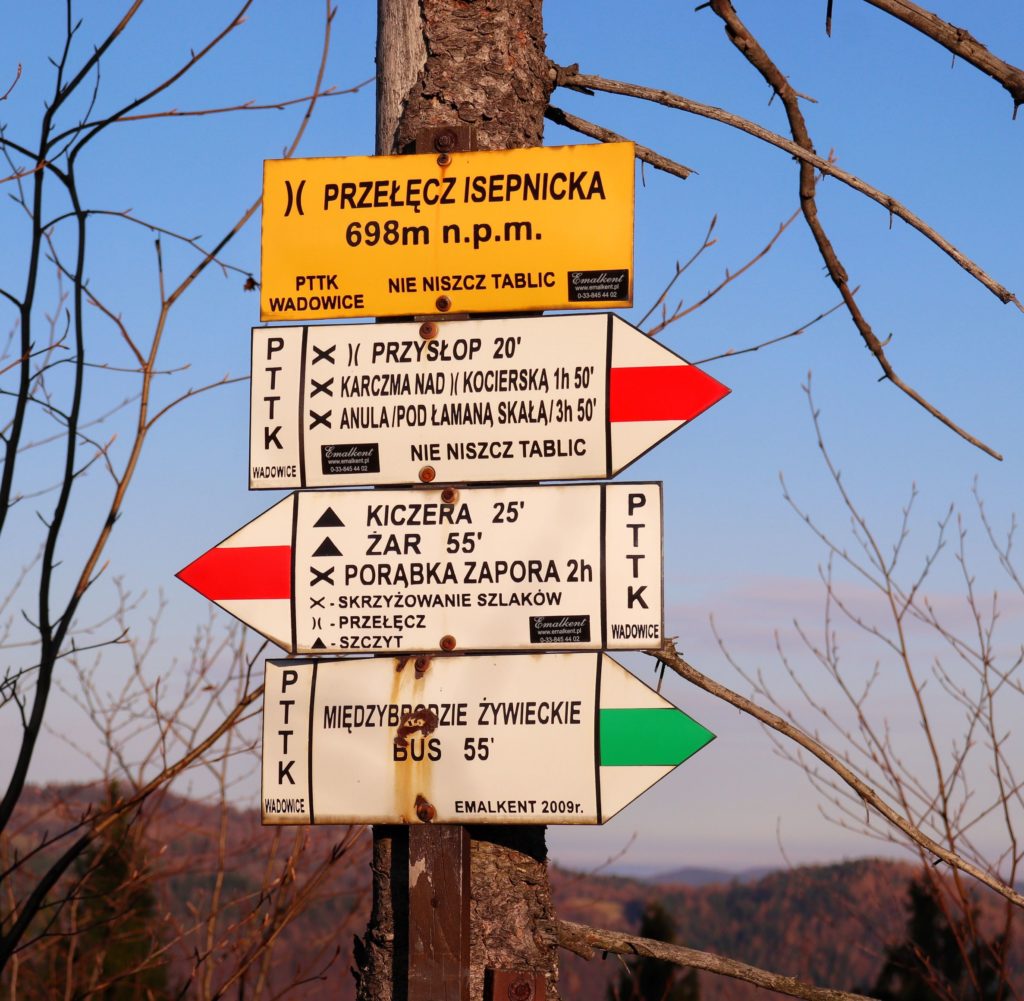 Słup z żółtą tablicą oznaczającą Przełęcz Isepnicka oraz białe tabliczki opisujące czerwony i zielony szlak