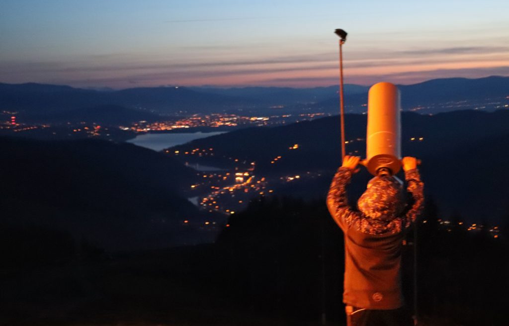 dziecko patrzące przez teleskop z Żaru, noc, ośwetlone w oddali miasta oraz jezioro