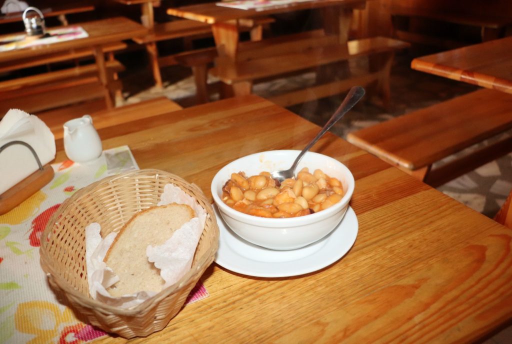 fasolka po bretońsku podana w białej miseczce, obok koszyczek z chlebem na drewnianym stole w schronisku PTTK na Hali Krupowej