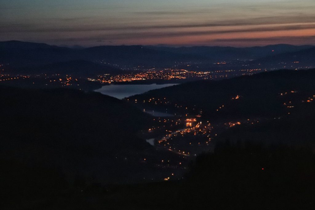 widok nocą z Góry Żar, w oddali oświetlone miasta, jezioro oraz krajobraz górski