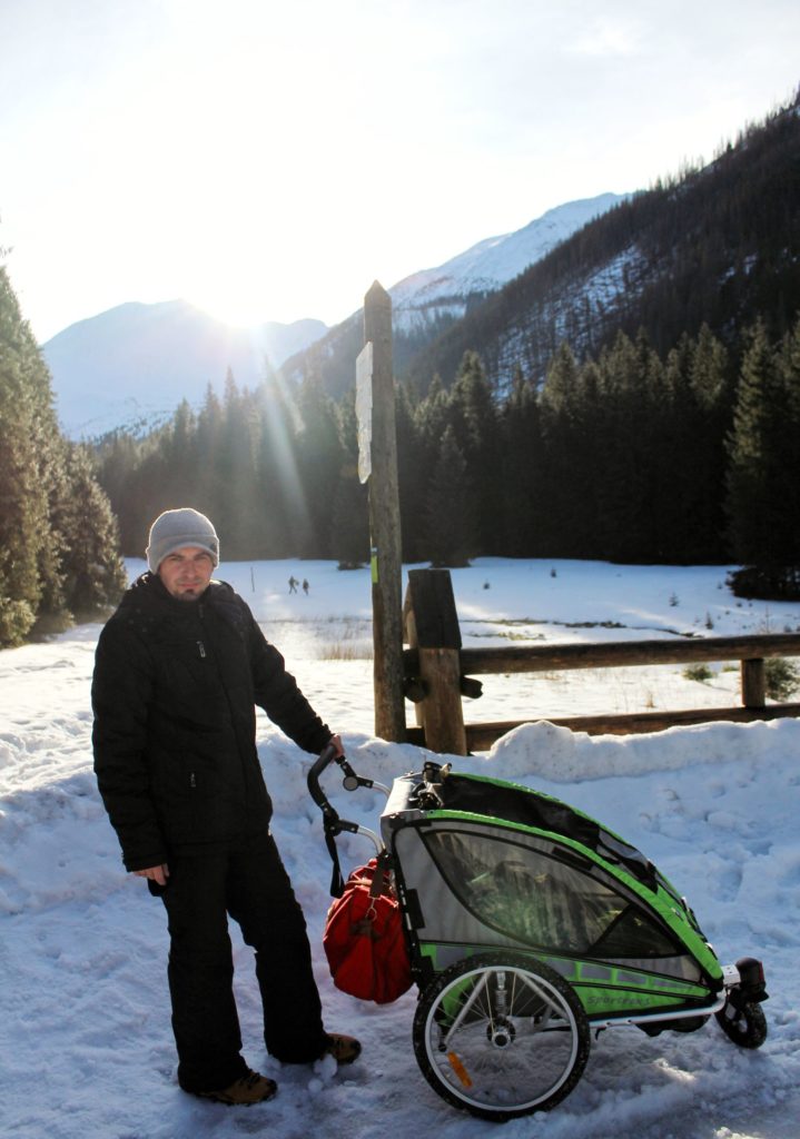 Hala Orank wózkiem, mężczyzna z dzieckiem w wózku na tle zimowych Tatr