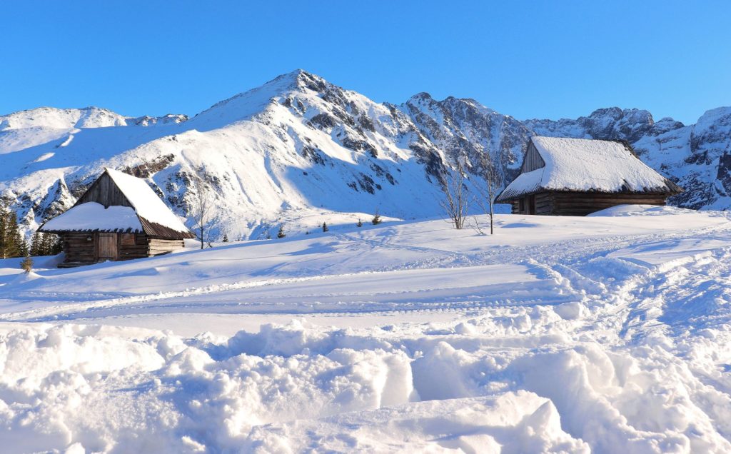 Ośnieżone, drewniane chaty na Hali Gąsienicowej na tle tatrzańskich szczyów, na hali zalega dużo świeżego śniegu