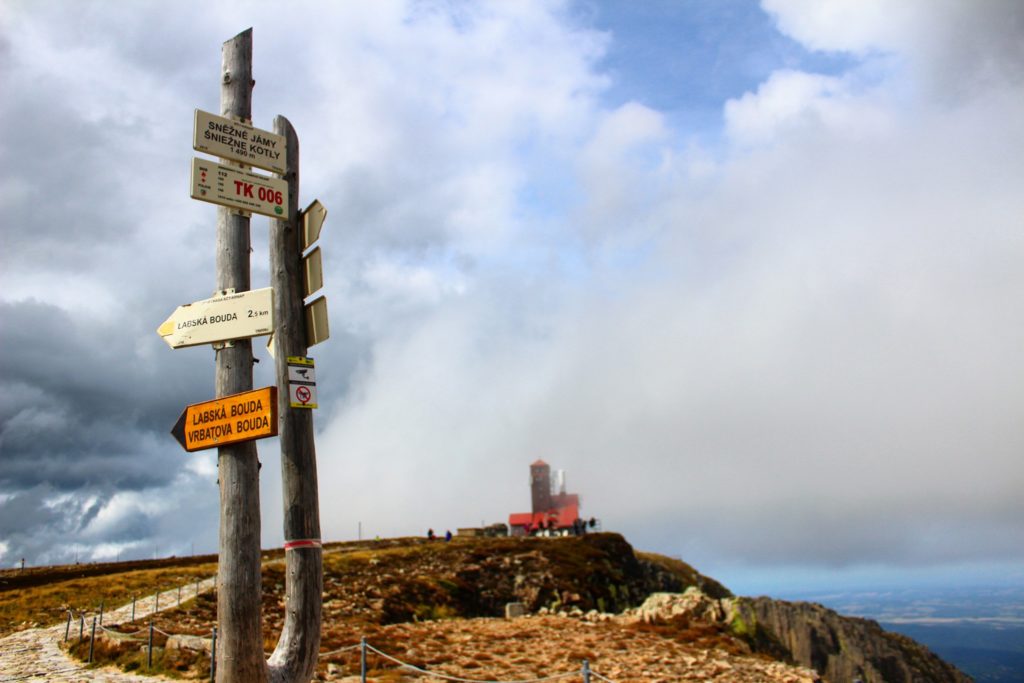 Słup z tabliczką oznaczającą szczyt Śnieżne Kotły leżące 1490 metrów nad poziomem morza, w tle widać drogę prowadzącą do budynku RTON na Śnieżnych Kotłach 