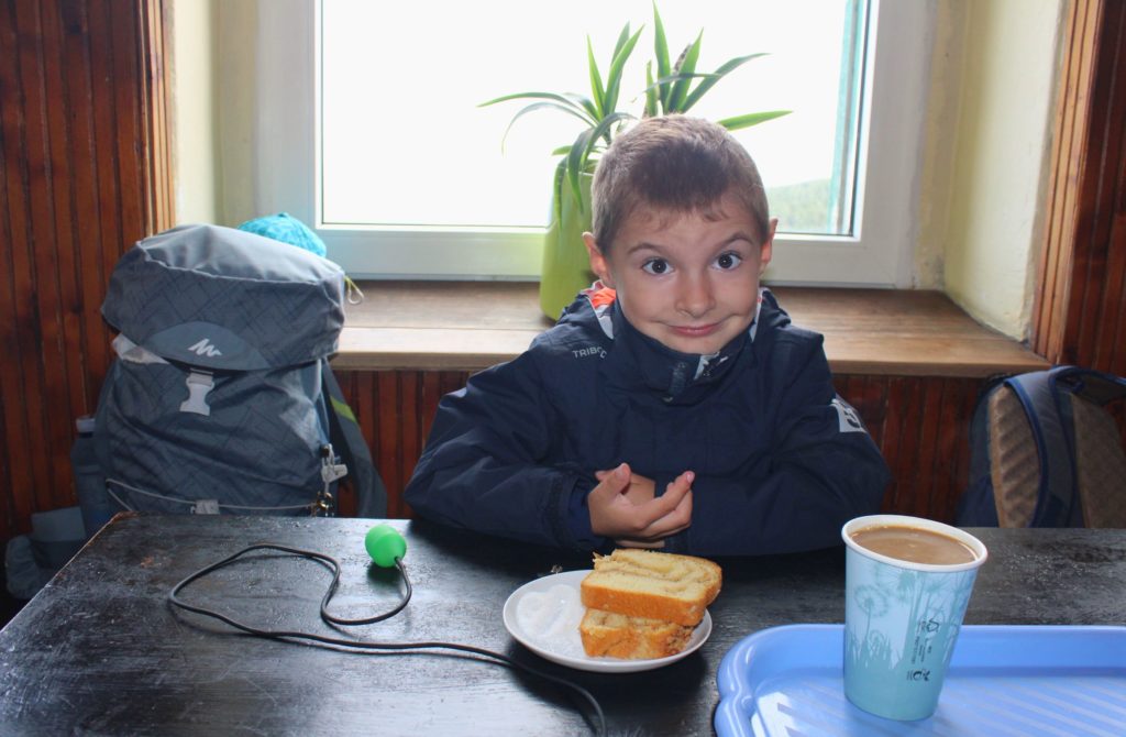 Uśmiechnięte dziecko siedzące przy stole w schronisku pod Łabskim Szczytem, na stole leży ciasto oraz kawa z mlekiem