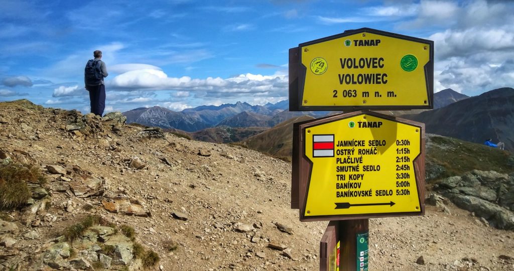 Szczyt Wołowiec, na którym umieszczona jest żółta tablica oznaczająca szczyt Wołowiec leżący 2063 metry nad poziomem morza na tle tatrzańskich szczytów