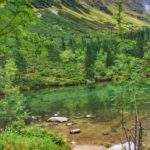 Brzeg Tatliakowego Jeziora, w oddali tatrzańskie szcyty, piękna, turkusowa woda w jeziorze, dużo zieleni na zdjęciu