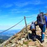 Dwójka turystów, mężczyzna z dzieckiem idący stromo w górę brukowaną drogą, błękitne niebo