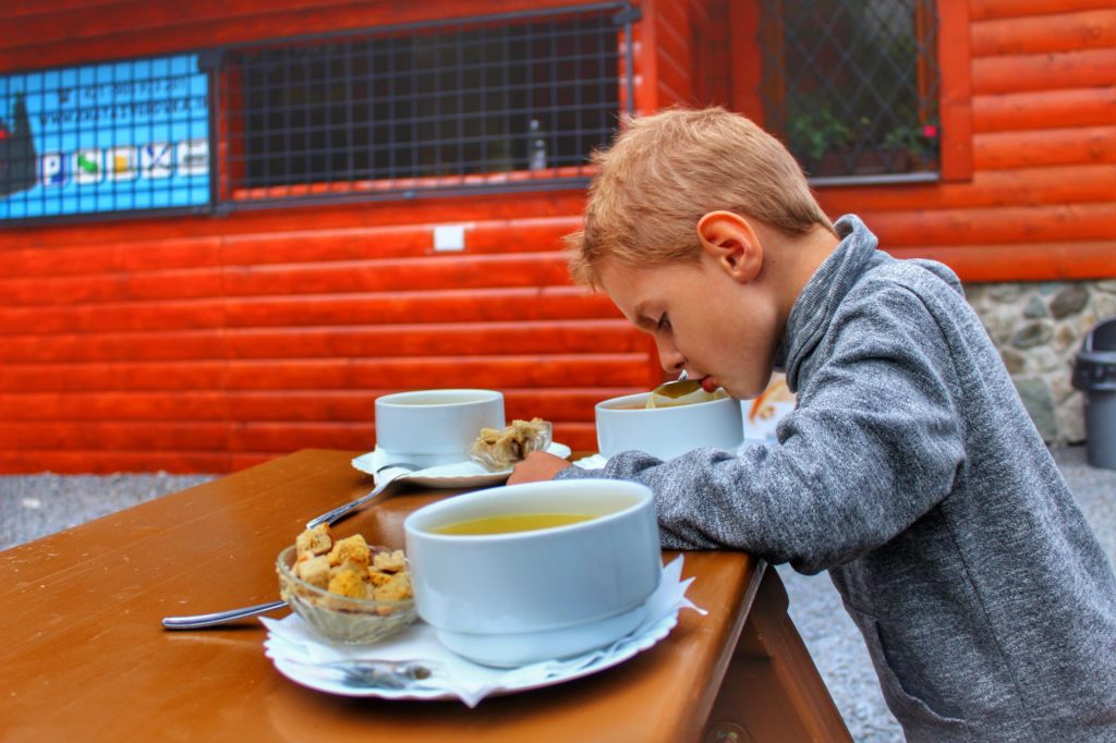 Dziecko siedząca przy drewnianym stole przy Bufecie Rohackim, jedzące zupę czosnkową z grzankami