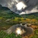 Piękne zachmurzone niebo, na którym jest słońce odbijające się w tafli Pośredniego Stawu Rohackiego