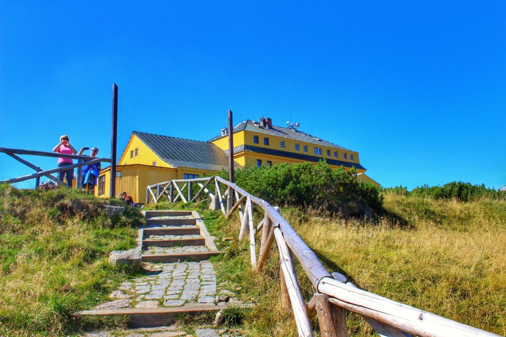 Schody prowadzące do schroniska Dom Śląski, żółty budynek, dwóch turystów robiących zdjęcia