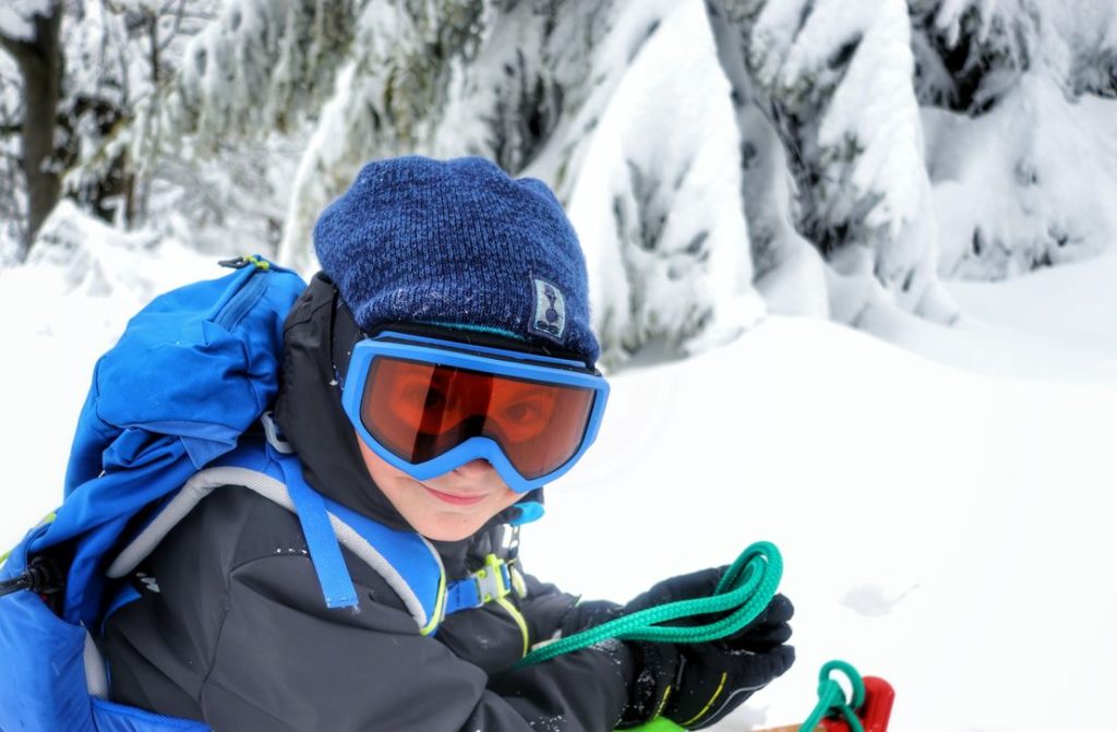 Szczęśliwe dziecko siedzące na sankach w goglach, w koło śnieg, iście zimowa sceneria