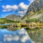 Słoneczny, wiosenny dzień, Wyżni Staw Rohacki odbijające się w tafli stawu szczyty Tatr oraz białe chmury