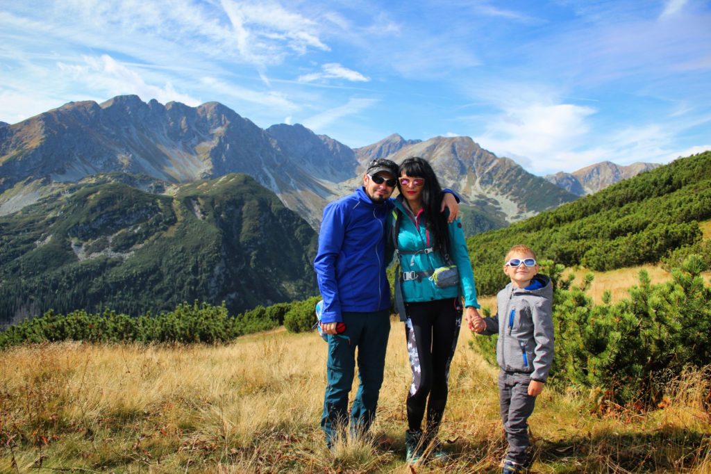 Trzyosobowa rodzina, w tym pięcioletnie dziecko na Zabratowej Przełęczy, w tle kosodrzewina oraz szczyty tatrzańskie, piękny, słoneczny dzień