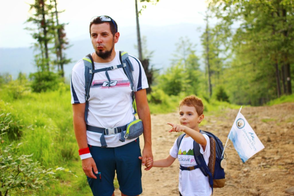 Turysta z dzieckiem na leśnej drodze, które pokazuje coś paluszkiem, na twarzach mężczyzny i dziecka zdziwienie