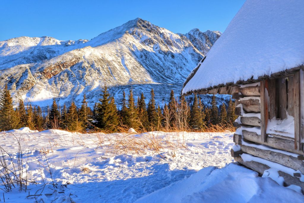 Drewniana chatka, widok na zaśnieżone Tatry z Hali Gąsienicowej