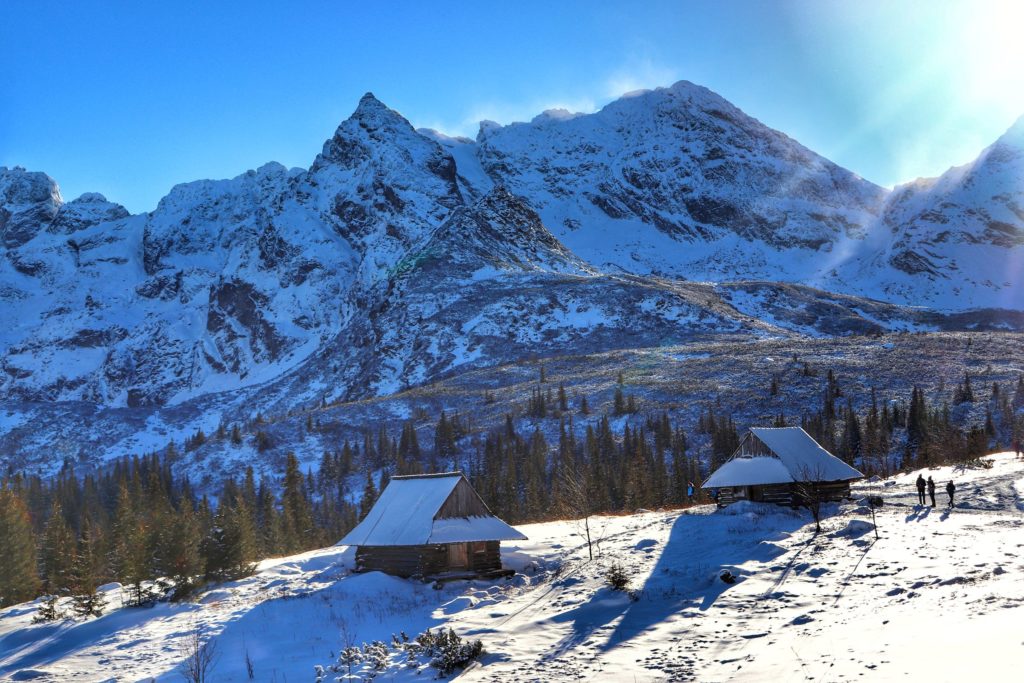 Drewniane chatki na zaśnieżonej Hali Gąsienicowej, widok na pokryte śniegiem tatrzańskie szczyty