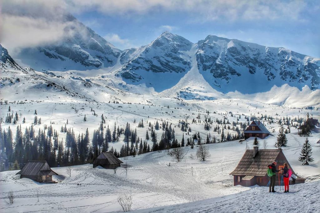 Hala Gąsienicowa zimą, drewniane chatki, zaśnieżone szczyty Tatr, turyści
