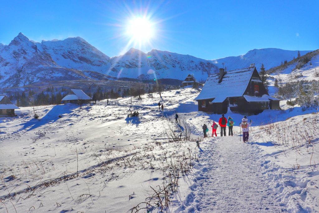Oświetlona przez popołudniowe słońce zimowa Hala Gąsienicowa, po prawej stronie Ośrodek szkolenia taterników Betlejemka, turyści