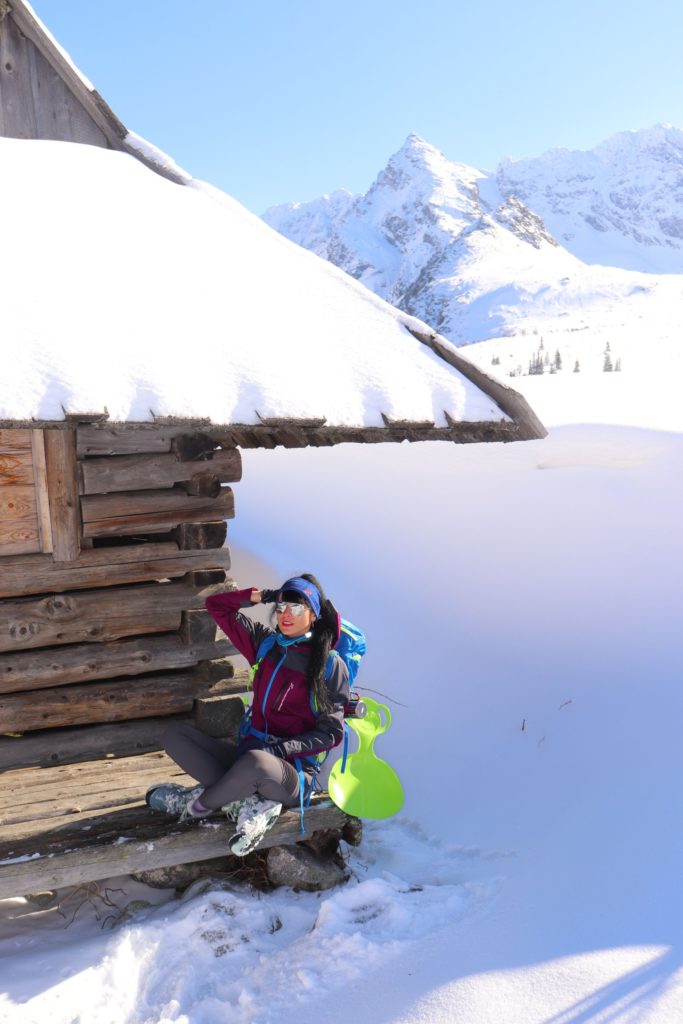 Turystka odpoczywająca pod zabytkowym, drewnianym domkiem na Hali Gąsienicowej, na której zalega dużo śniegu