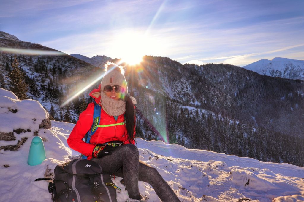 Uśmiechnięta turystka odpoczywająca na niebieskim szlaku idącym do Przełęczy między Kopami, w tle tatrzańskie szczyty, zima